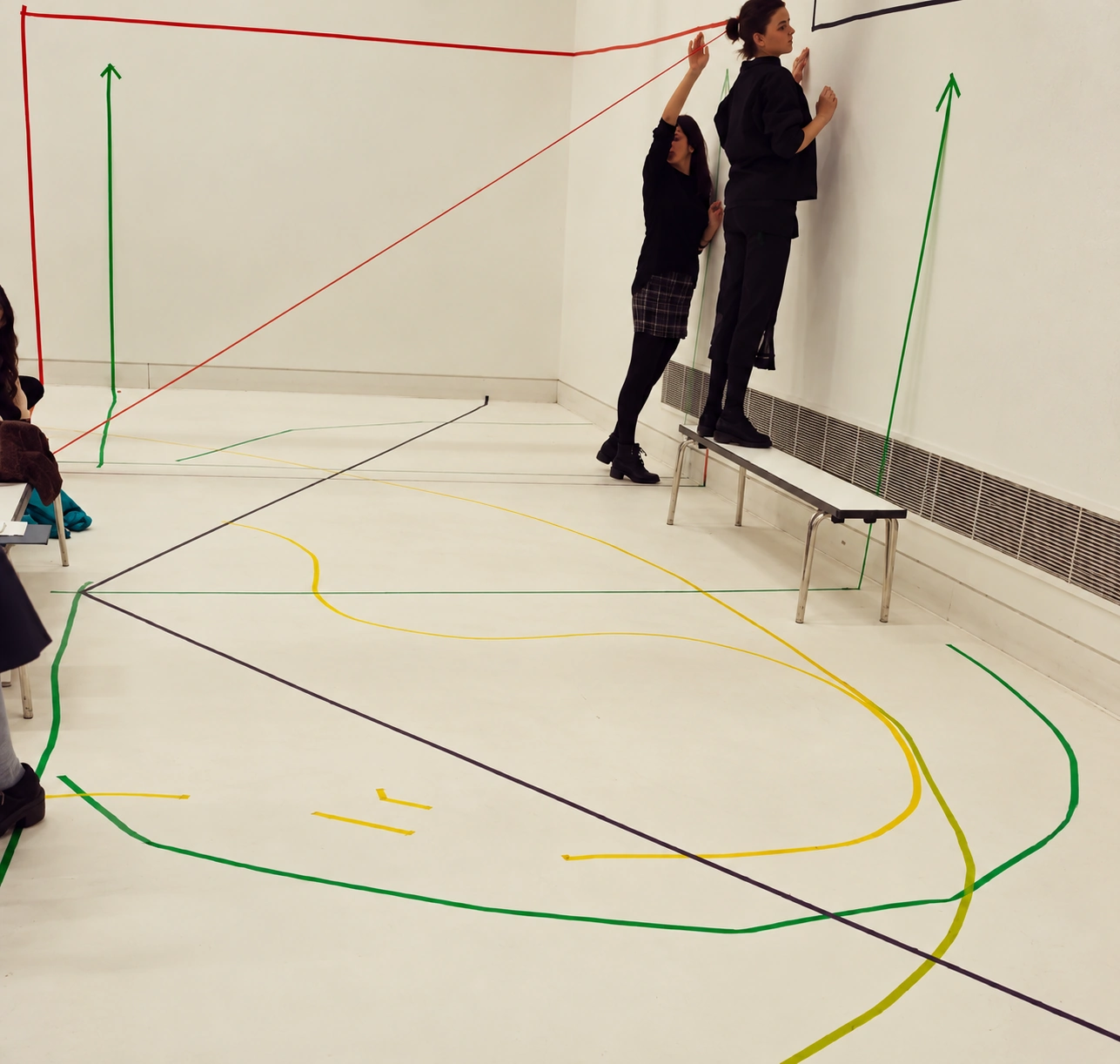 Performers stretching coloured lines across a white room and around a bench